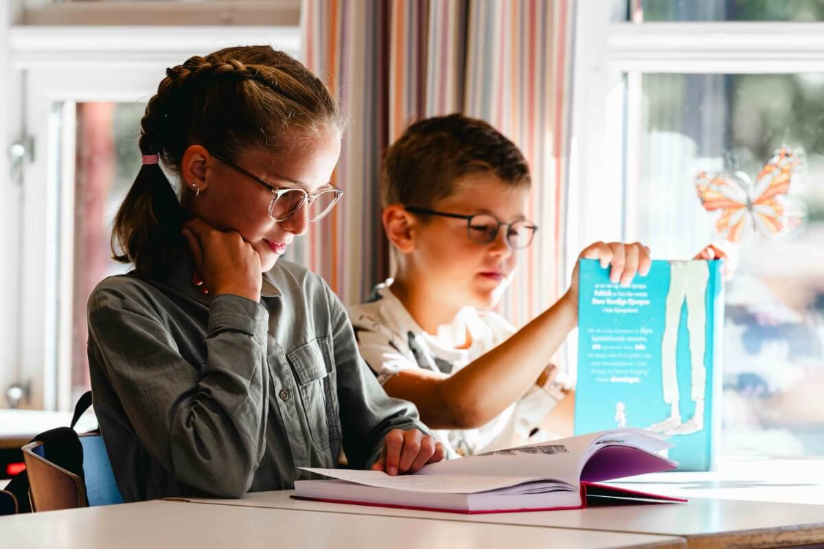 Jente og gutt med briller sitter i klasserom og leser
