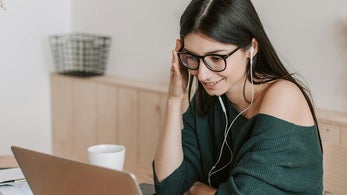 Student med briller foran datamaskin ser på skjermen til smarttelefonen